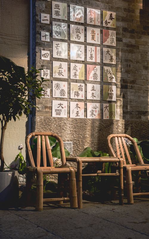 Free Bamboo chairs in front of a brick wall adorned with Chinese calligraphy cards in a serene outdoor setting. Stock Photo