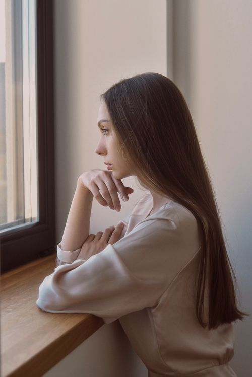 Free Young woman lost in thought gazing through a window, conveying introspection. Stock Photo