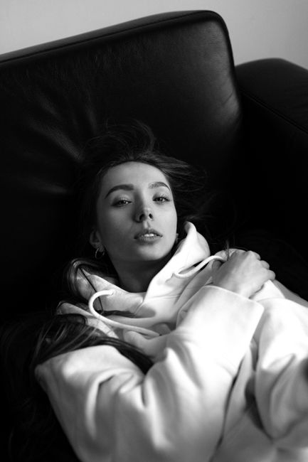 Elegant black and white portrait of a woman reclining on a leather sofa indoors.