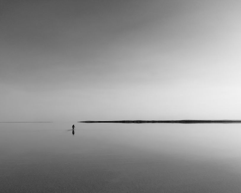 A lone figure stands in tranquil waters beneath a vast, serene sky, embodying solitude and reflection.
