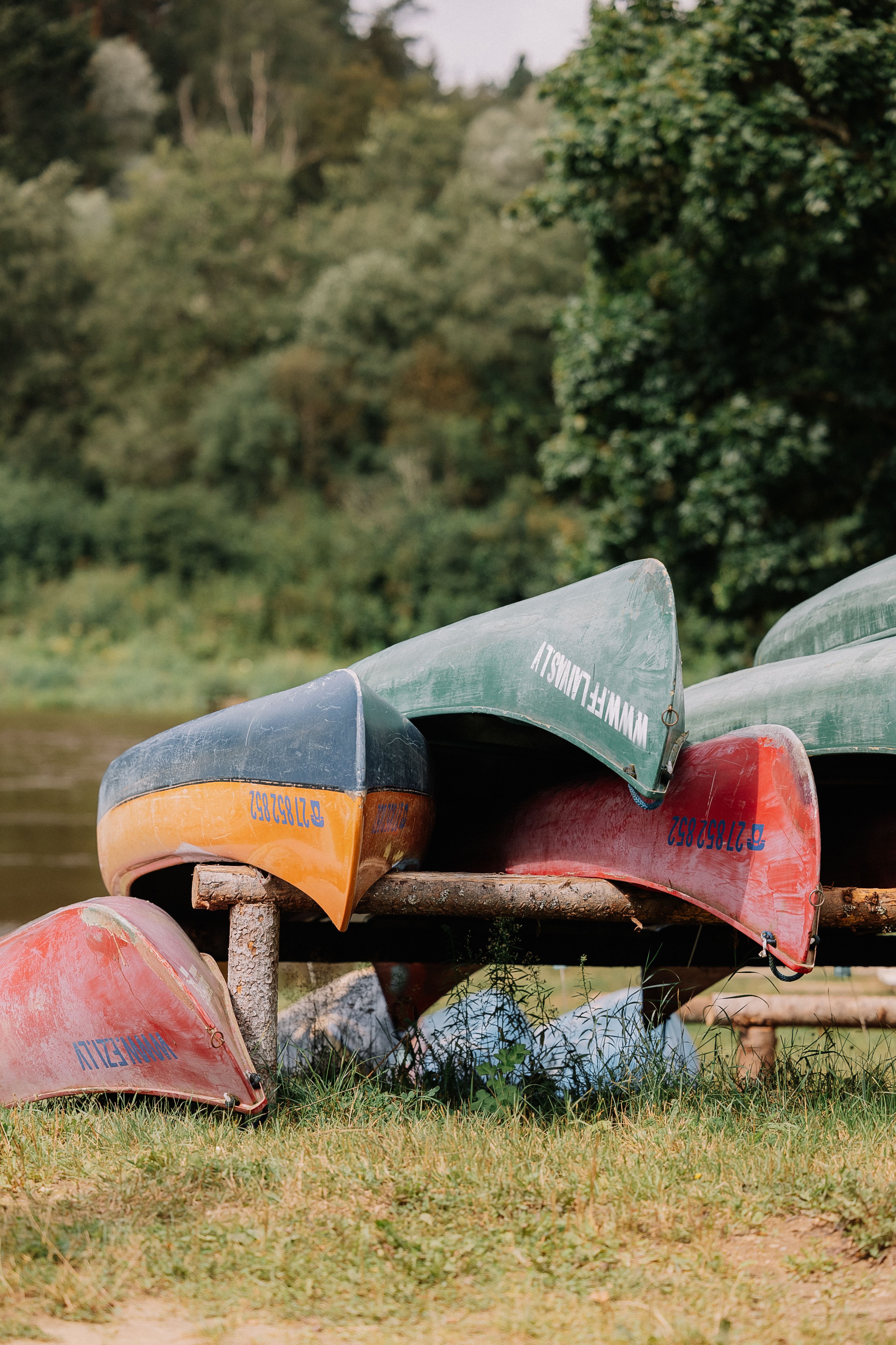 Colorful canoes stacked near a tranquil riverbank amidst lush greenery.