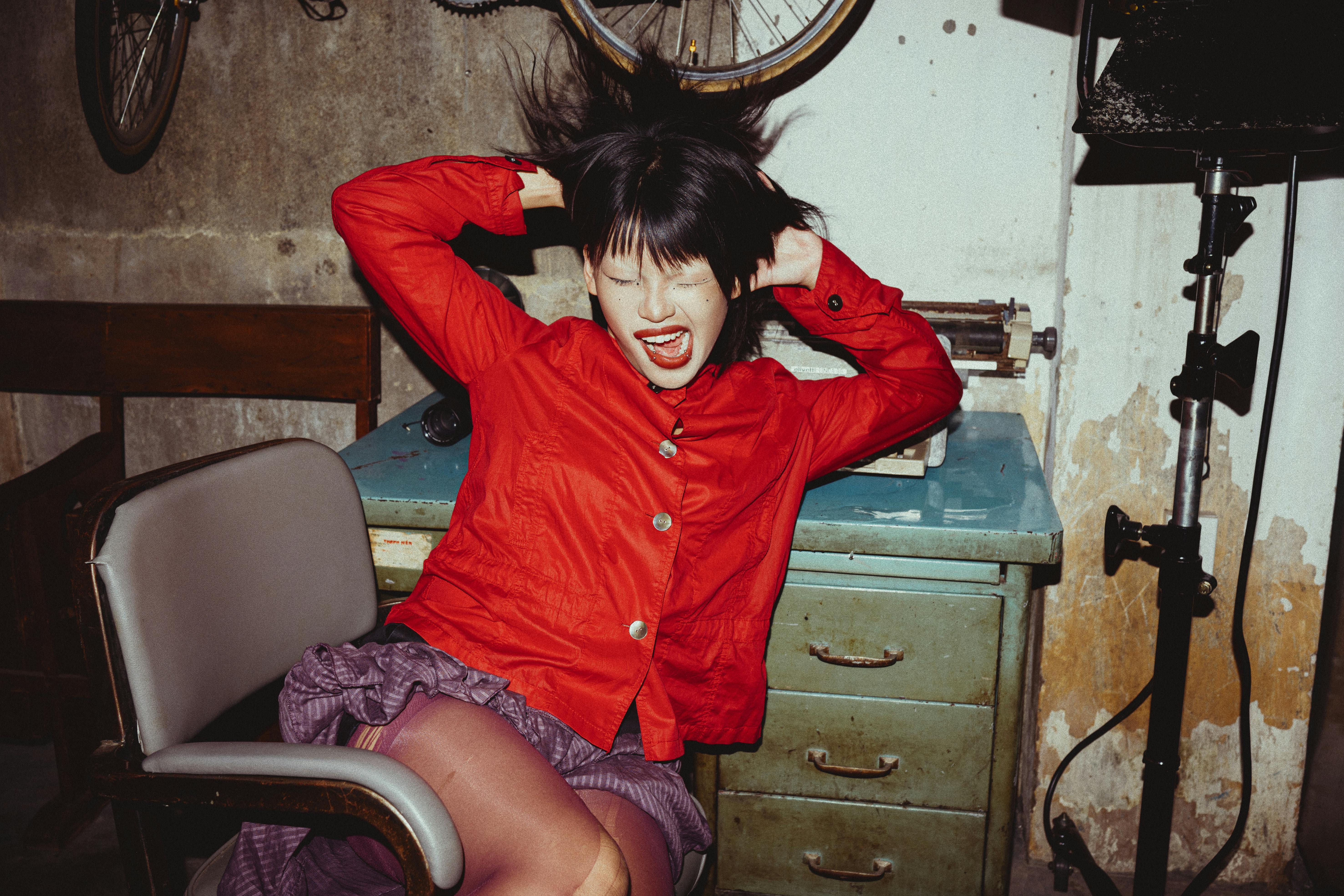 Expressive young woman in red shirt posing dramatically indoors.