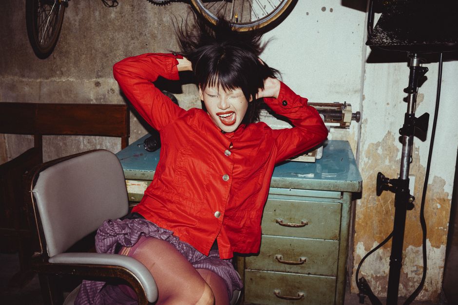 Expressive young woman in red shirt posing dramatically indoors.
