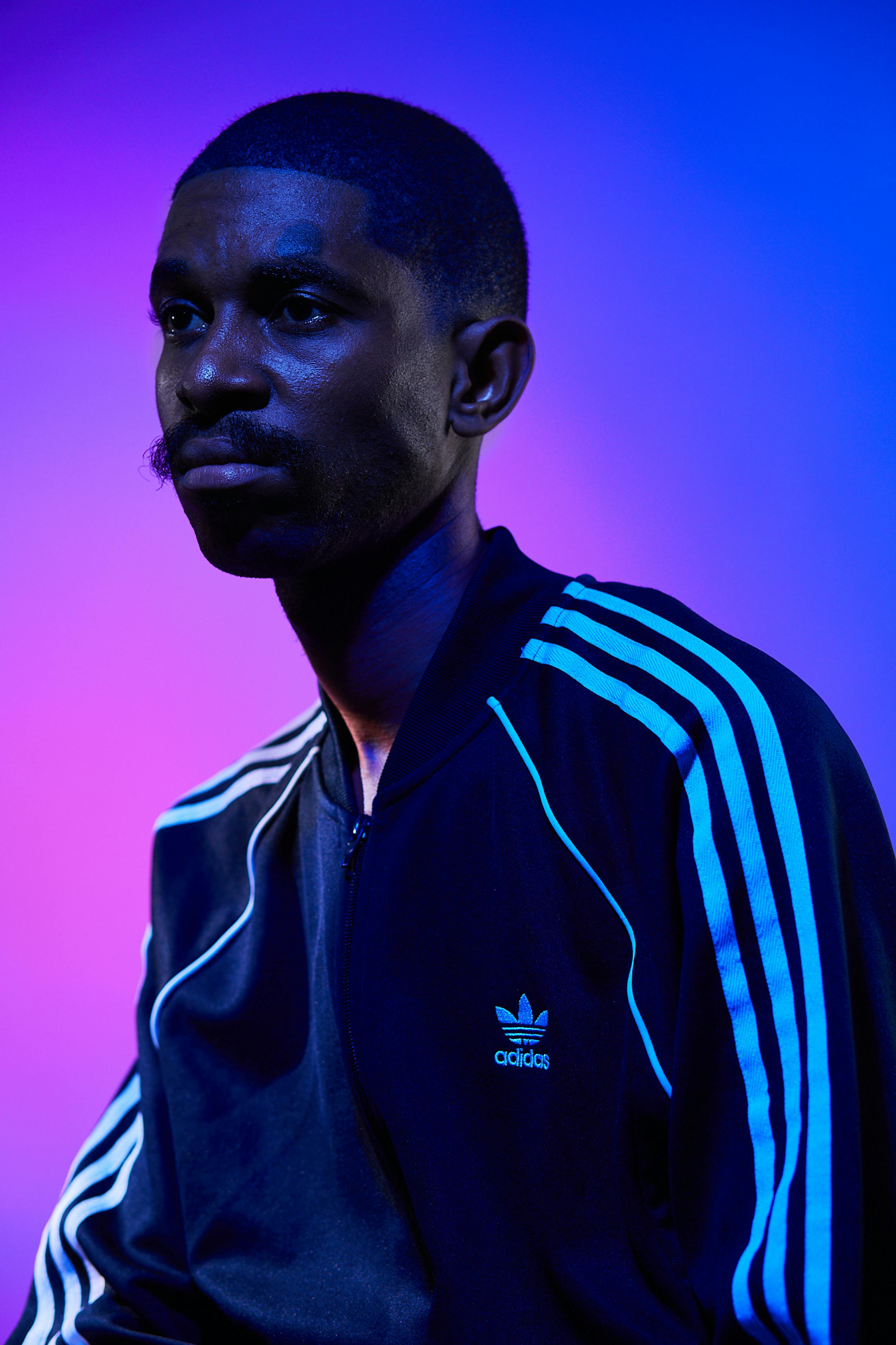 Portrait of a man in a dark Adidas jacket with vibrant blue and purple lighting. Artistic view.