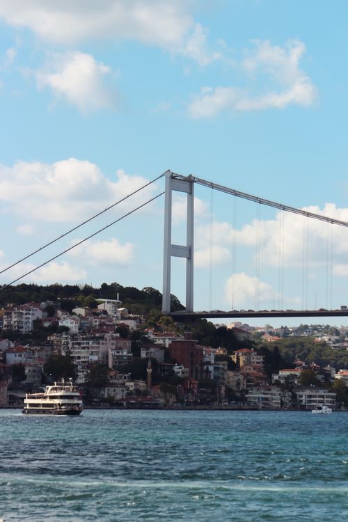 Free Scenic view of the Bosphorus Bridge and waterfront with a ferry, capturing urban and maritime elements. Stock Photo