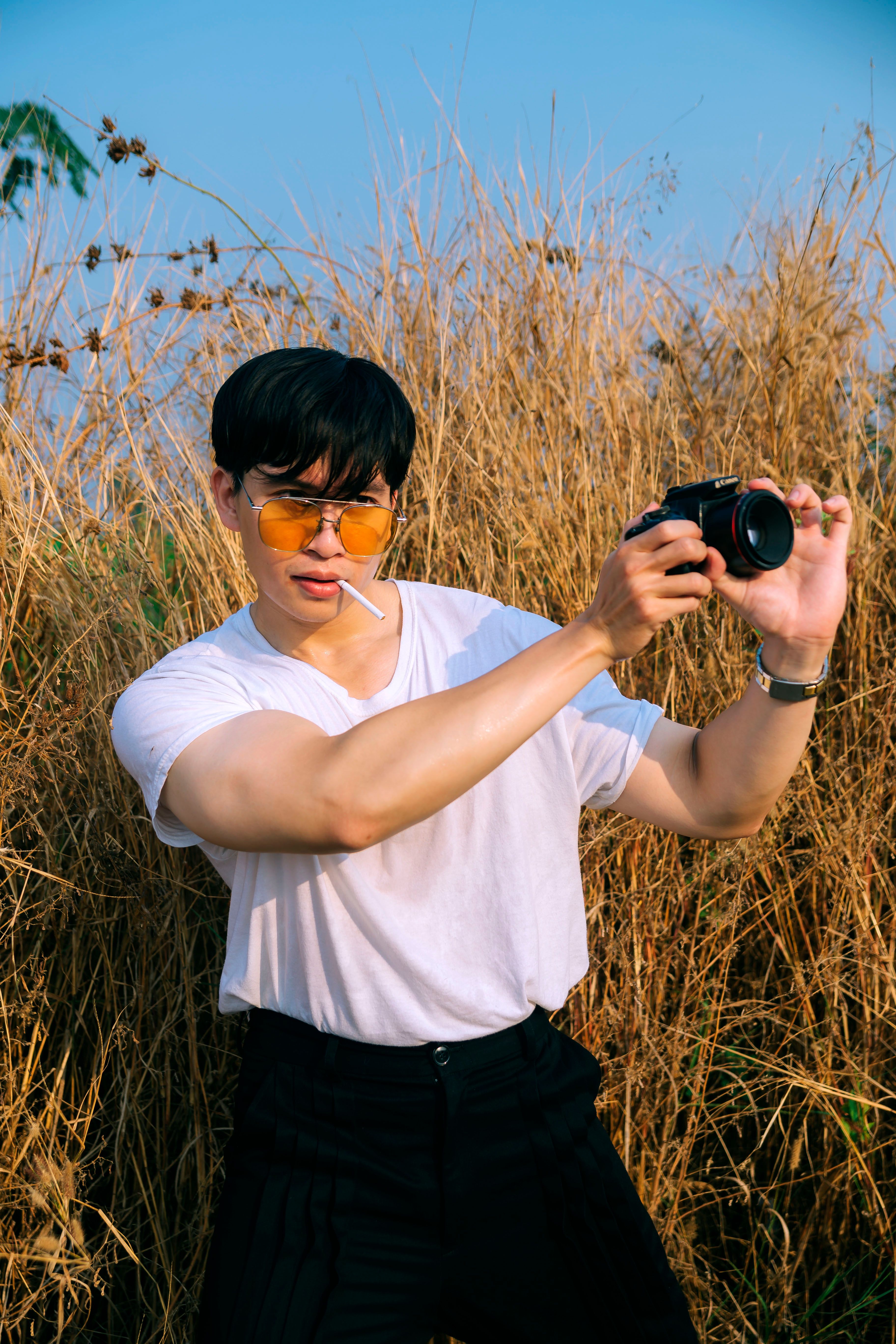 A stylish man with sunglasses takes photos in a grassy field during sunset.