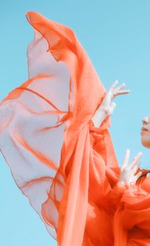 Elegant woman in a flowing silk scarf poses against a vibrant summer sky.