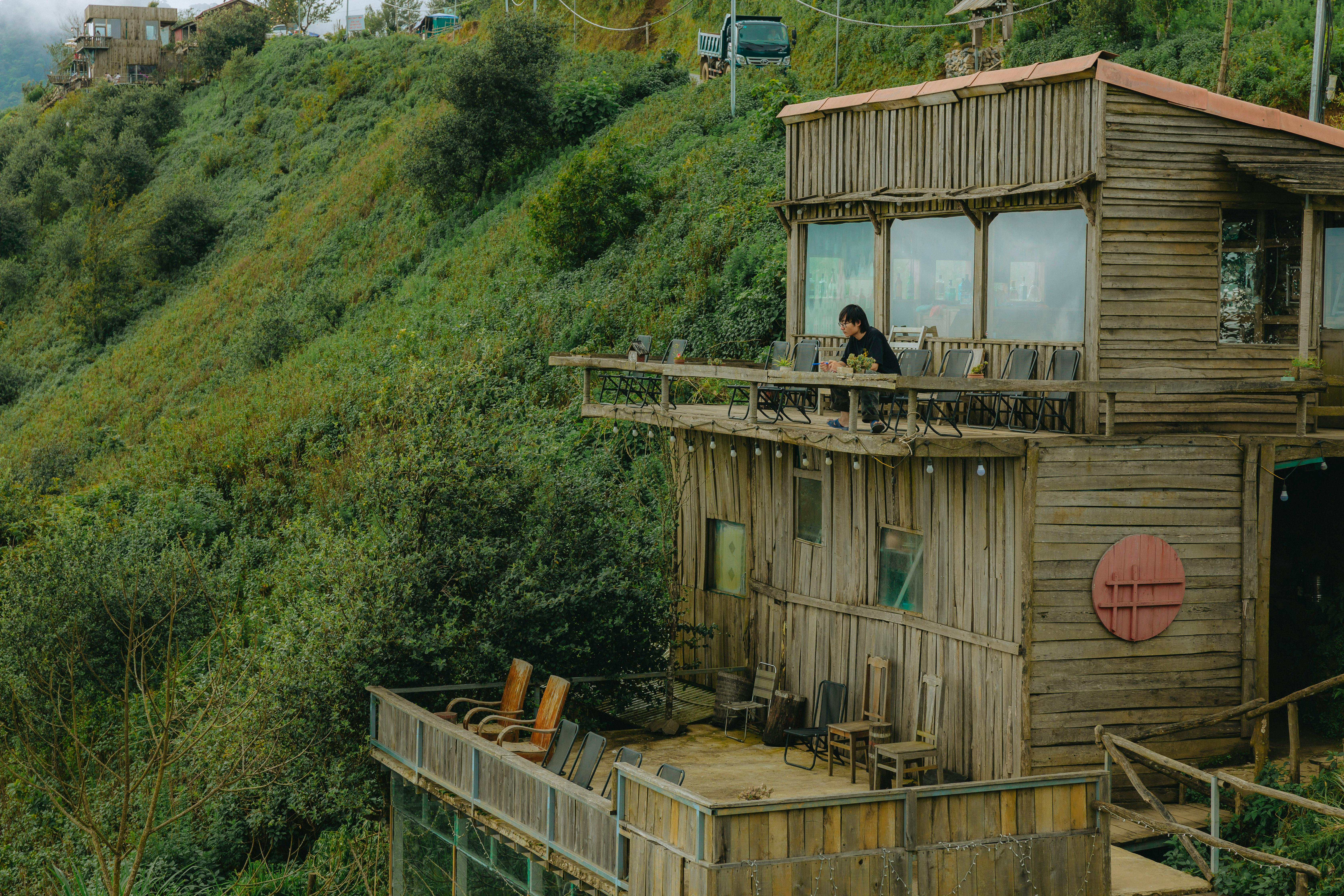 a wooden house on top of a hill with a person sitting on the roof