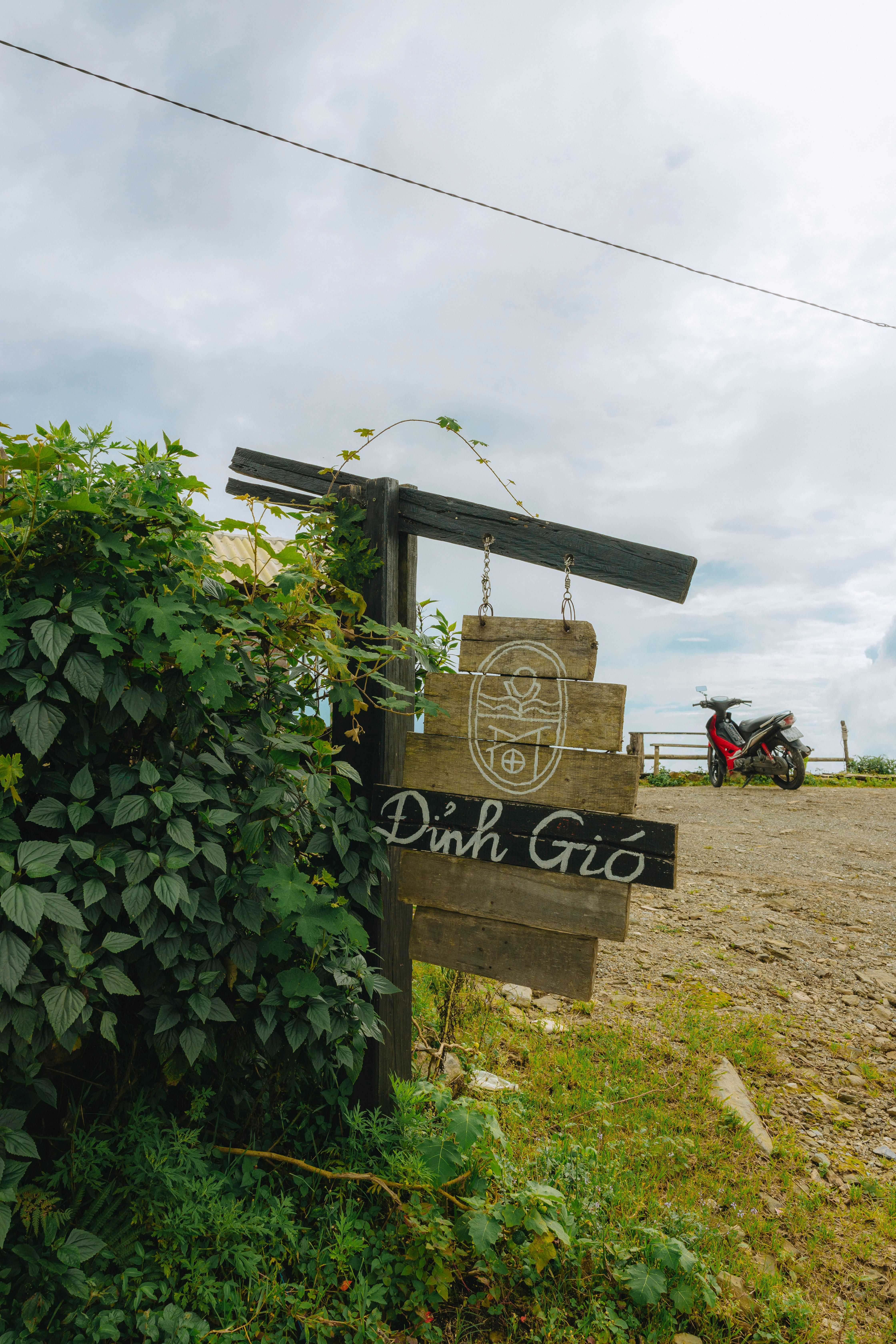 A wooden sign marked 'Dinh Gio' with a rural landscape and a parked motorcycle.