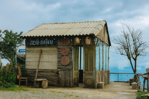 Free A charming rustic wooden hut set against a rural background with trees and sky. Stock Photo