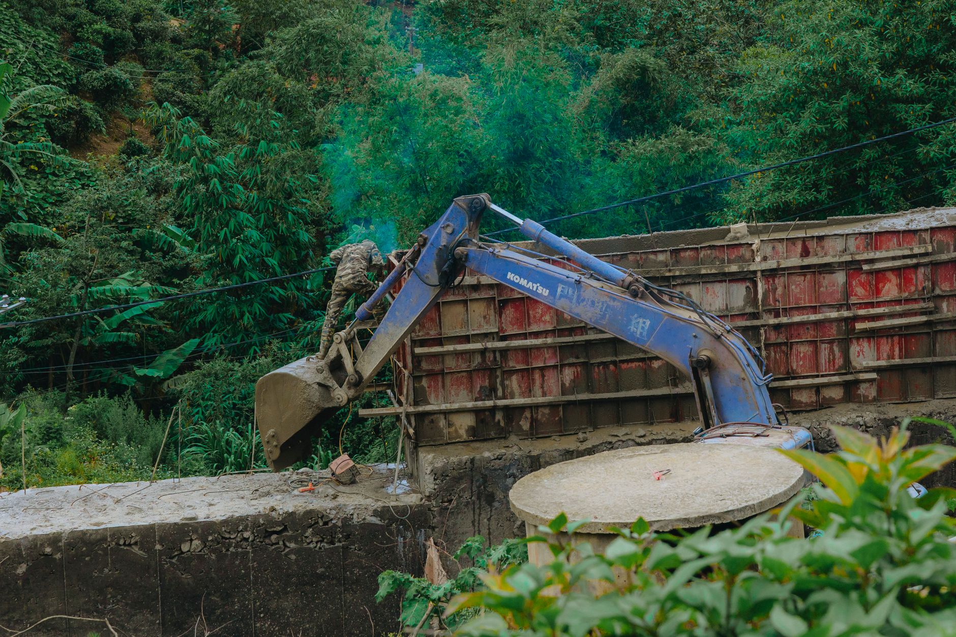 An excavator operates amidst dense greenery, highlighting machinery in nature.