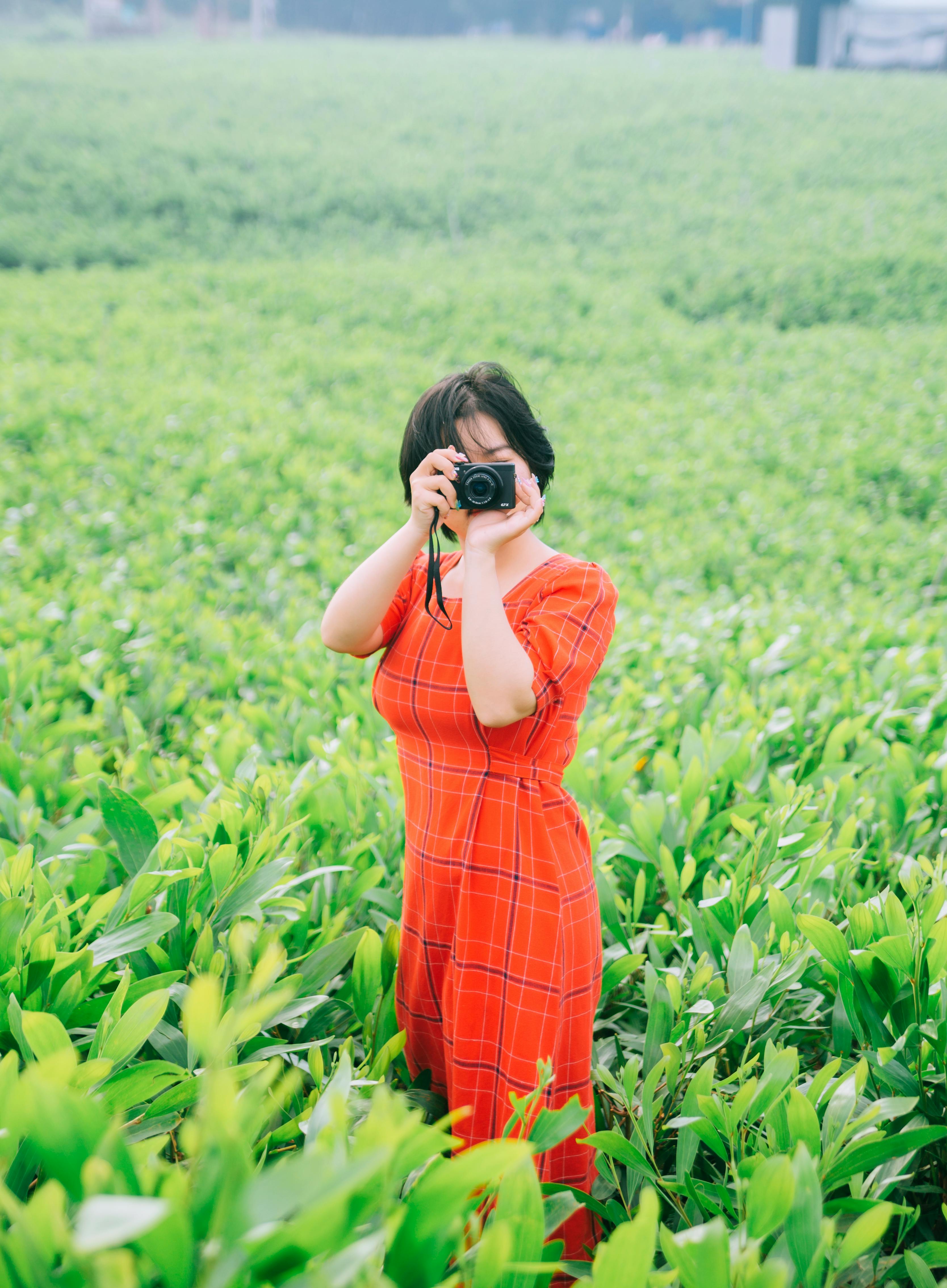 A woman in a red dress taking a photo in a vibrant green field.