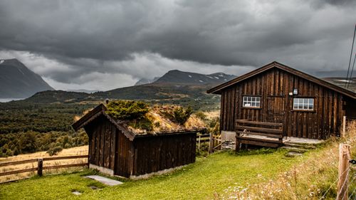 Free Wooden cabins on a green hill under cloudy skies with mountains in the background. Stock Photo