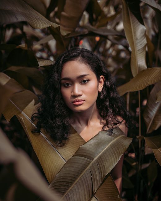 Beautiful portrait of a woman amidst tropical leaves in Kuala Lumpur's vibrant nature.