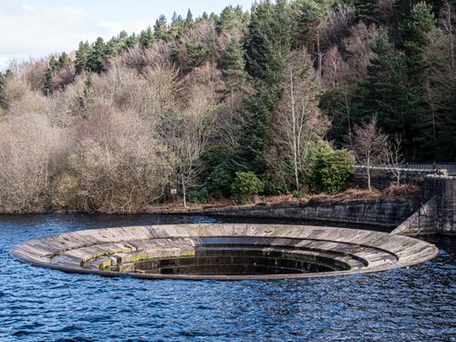 Free Dramatic water overflow structure in a reservoir surrounded by lush forest. Stock Photo
