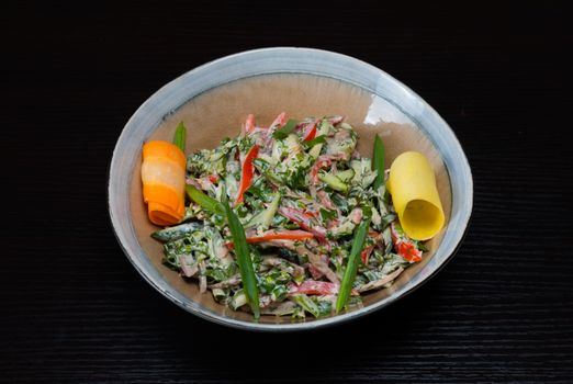 A colorful vegetable salad with carrot and zucchini garnishes in a ceramic bowl on a dark background.