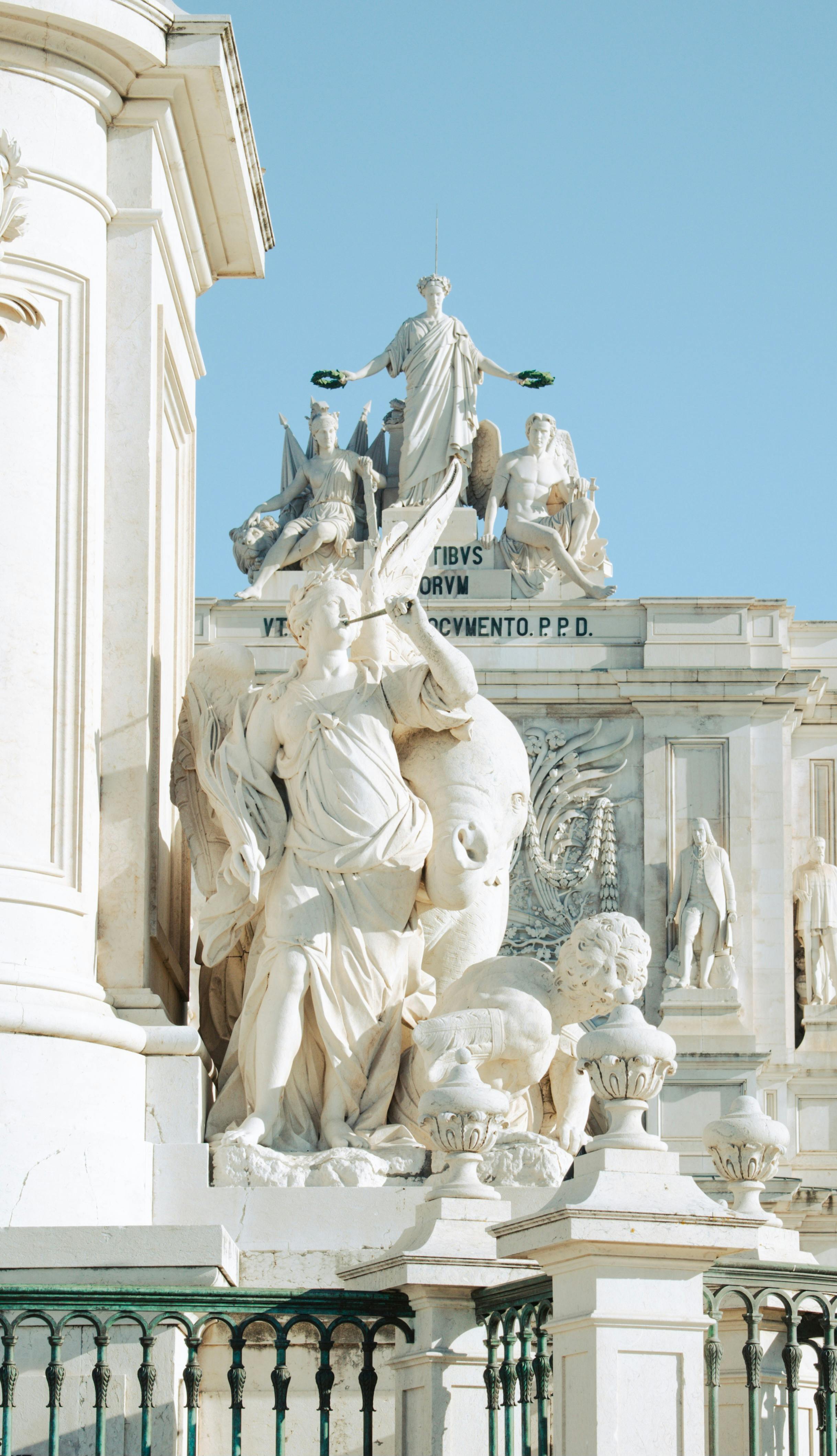 Statues of a baroque monument in Lisbon against a clear blue sky, showcasing historic architecture.
