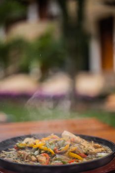 A steaming mixed vegetable dish served outdoors on a rustic wooden table.