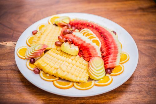 Free Vibrant fruit platter featuring watermelon, oranges, pineapple, apples, and grapes on a wooden table. Stock Photo