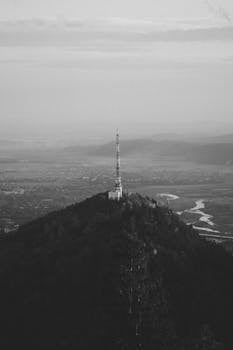 Monochrome aerial photograph capturing a tower on a mountain peak surrounded by mist.