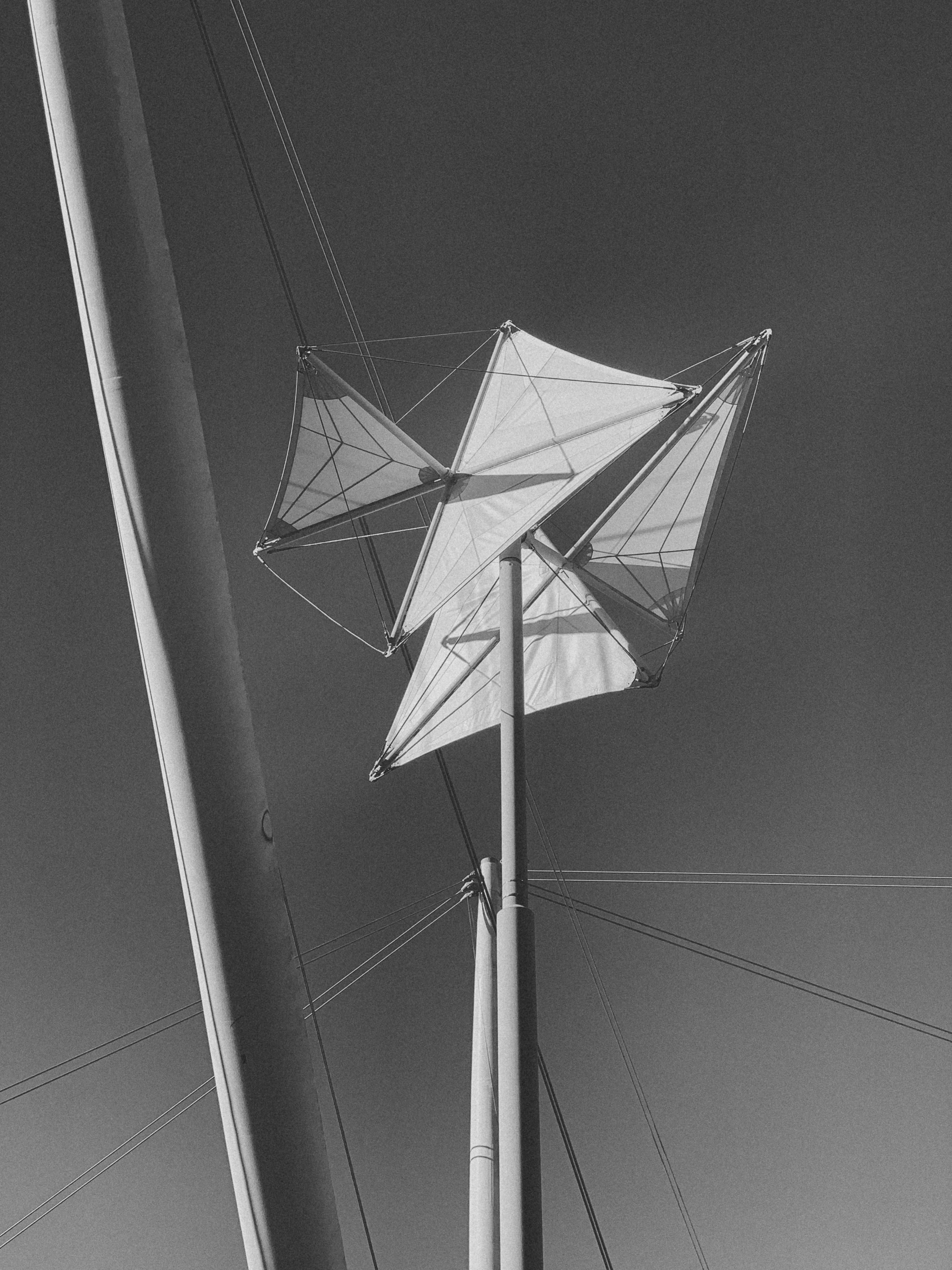Close-up of a sailboat mast with sails in black and white under clear sky.