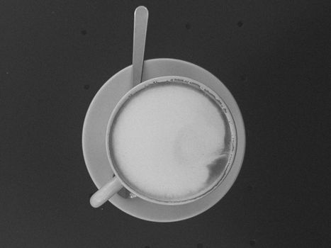 Black and white aerial shot of a cappuccino with foam art in a cup and saucer.