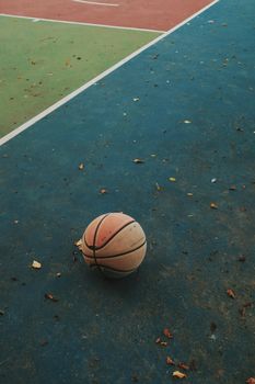 A lone basketball rests on a vibrant outdoor court with scattered leaves, capturing an urban sports vibe.