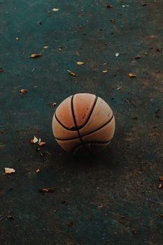 A lone, weathered basketball on an outdoor urban court with scattered leaves.