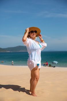 A woman in a sun hat and cover-up enjoys a sunny day on a tropical beach, showcasing relaxation and leisure.