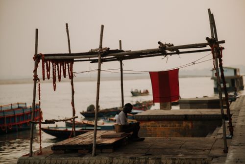 Free A tranquil harbor scene featuring fishing boats, a pier, and a lone figure under a makeshift shelter. Stock Photo