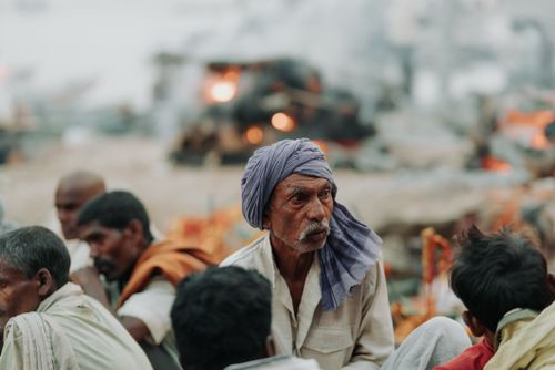 Free A group of men sit together at a cultural site with fires burning in the background, showcasing traditional clothing and customs. Stock Photo