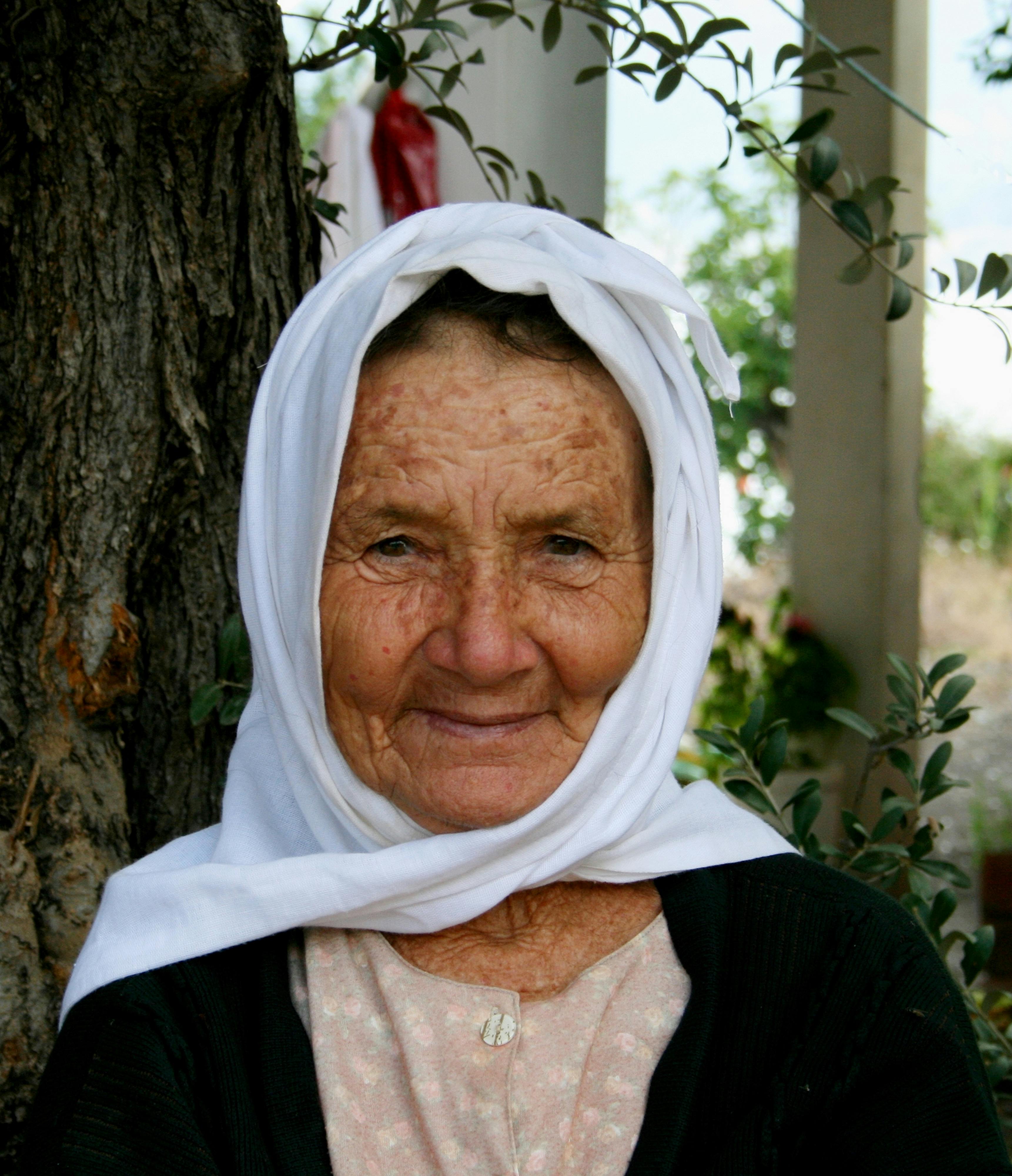 Captivating portrait of a senior woman with a white headscarf in a natural outdoor setting.