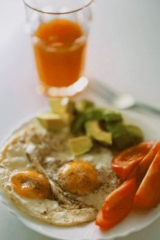 Delicious breakfast featuring eggs, avocado, and tomatoes with orange juice.