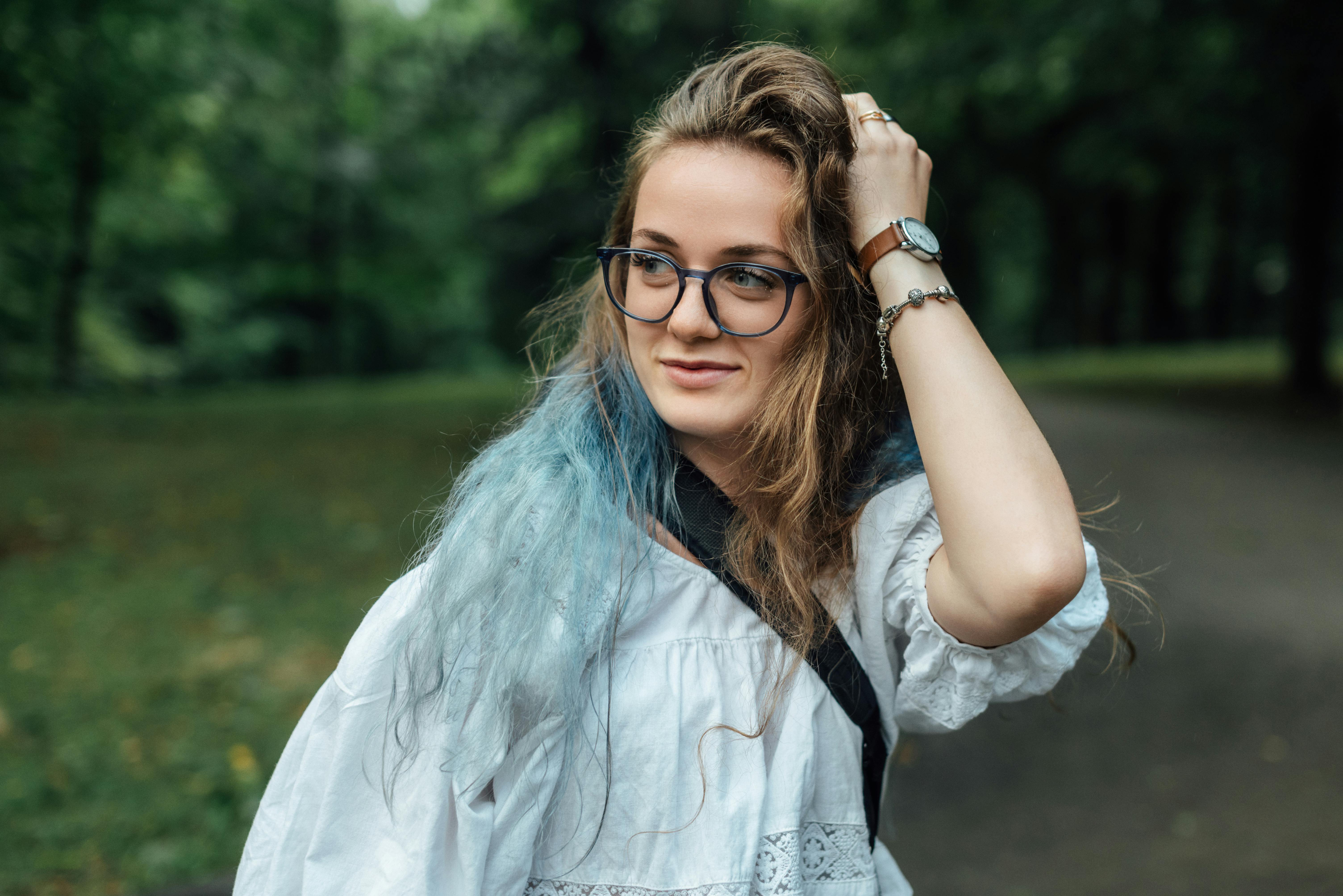 A stylish young woman with glasses and long hair enjoys a sunny day in the park.