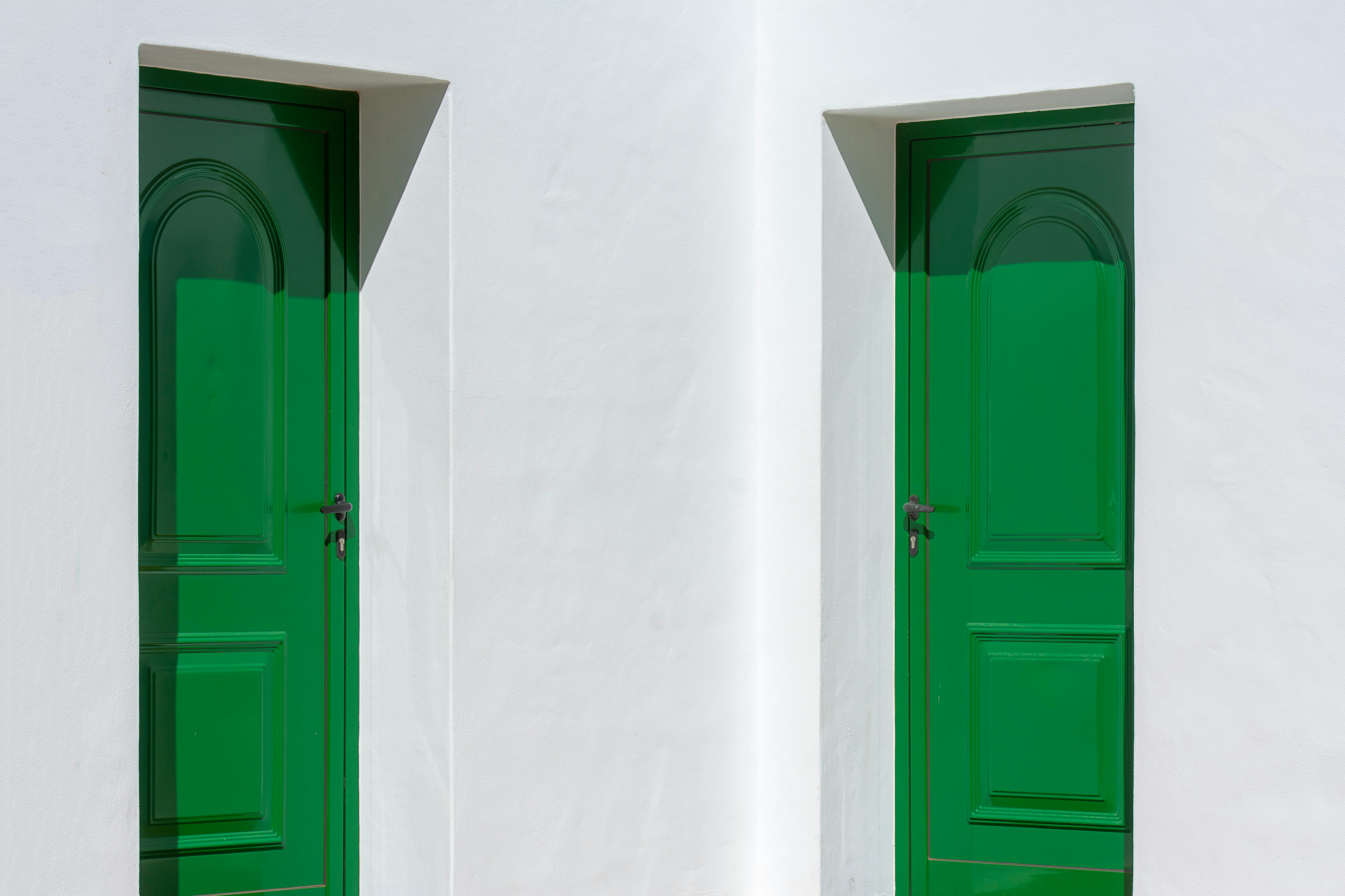 Minimalist architecture with two bright green doors on a white wall, showcasing a modern aesthetic.