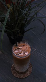 Chilled coffee drink with ice cubes on a wooden table beside a plant.