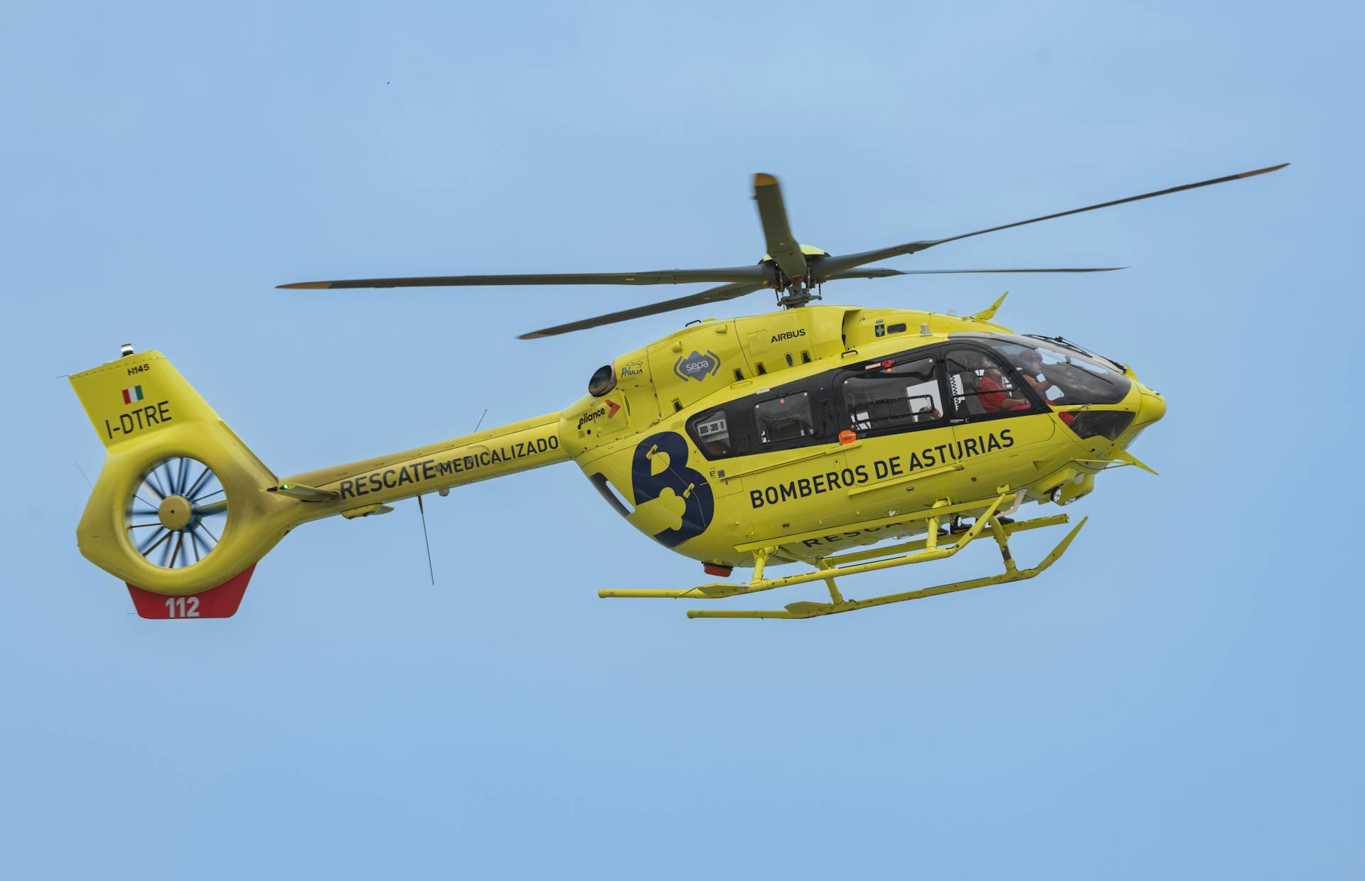 A yellow helicopter flying in the sky with a person on board