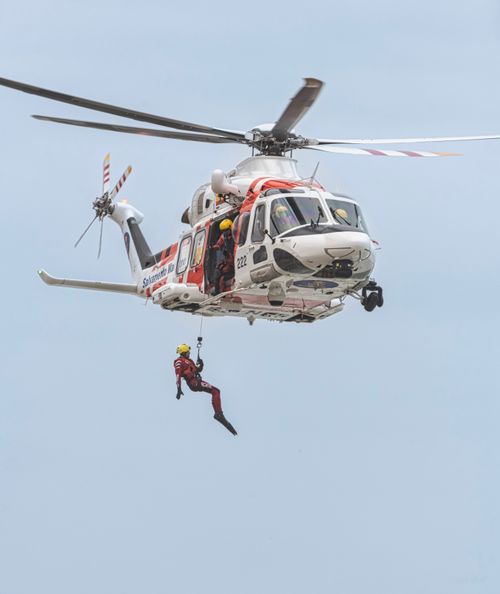 Free A dramatic helicopter rescue operation featuring a suspended rescuer in mid-air, showcasing emergency response readiness. Stock Photo
