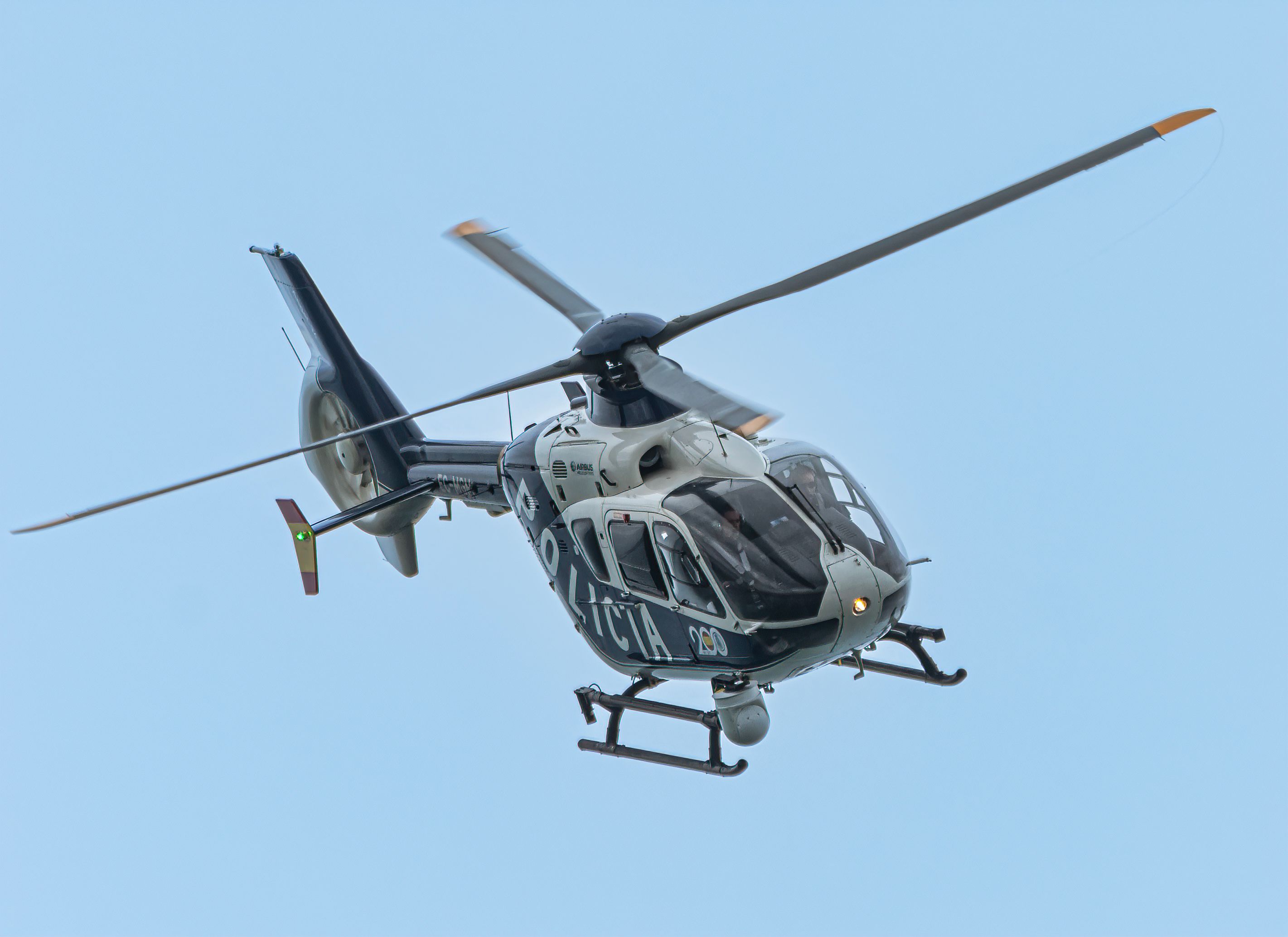 A police helicopter in mid-flight with a clear blue sky backdrop. Captured in high detail.