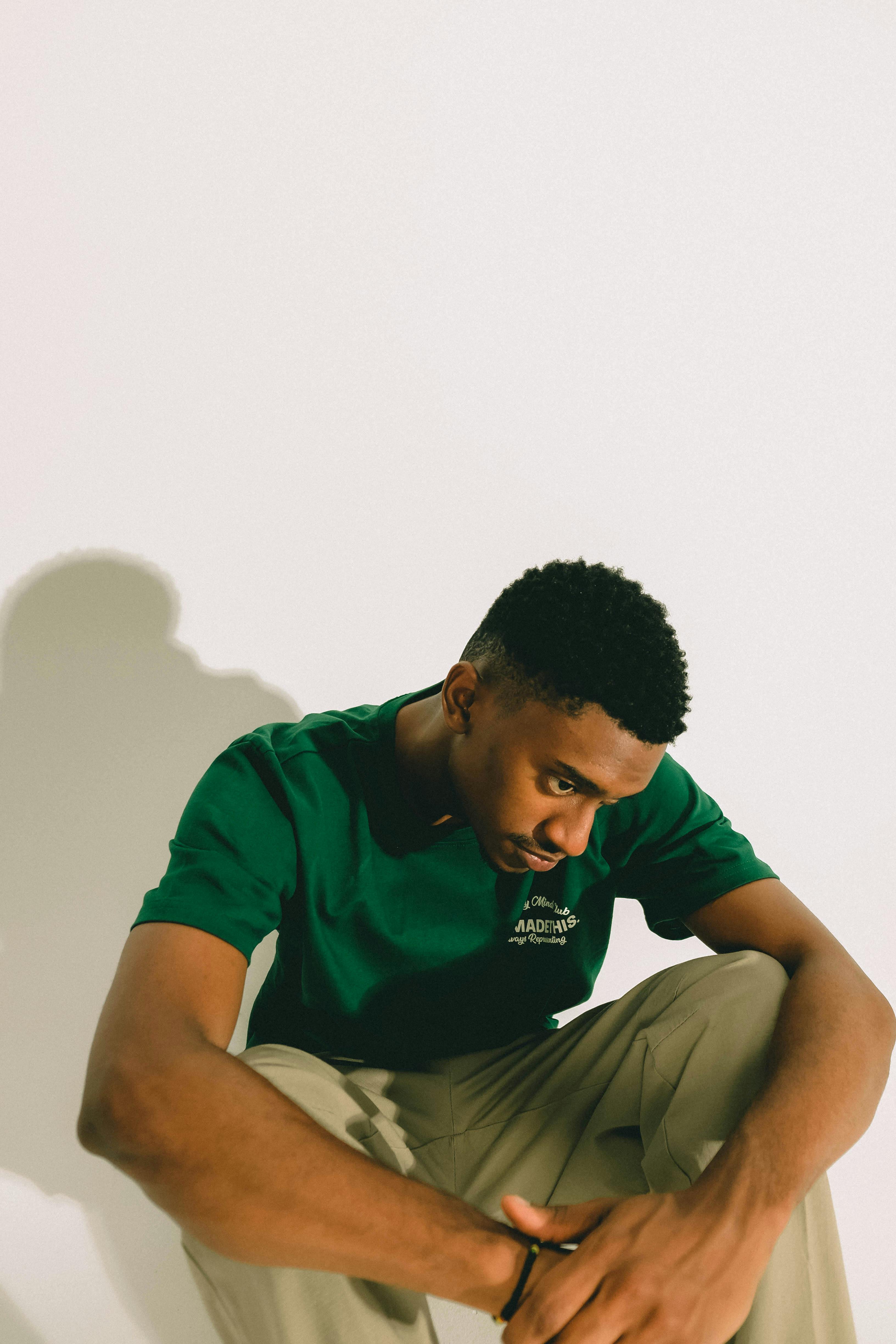 Young man in a green shirt sitting contemplatively in a bright studio.