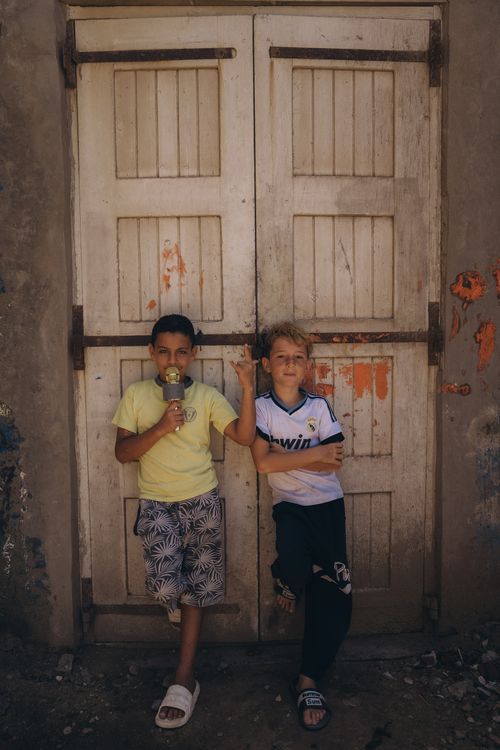 Free Two young boys leaning against a weathered door in Kafr El-Shaikh, Egypt on a sunny day. Stock Photo
