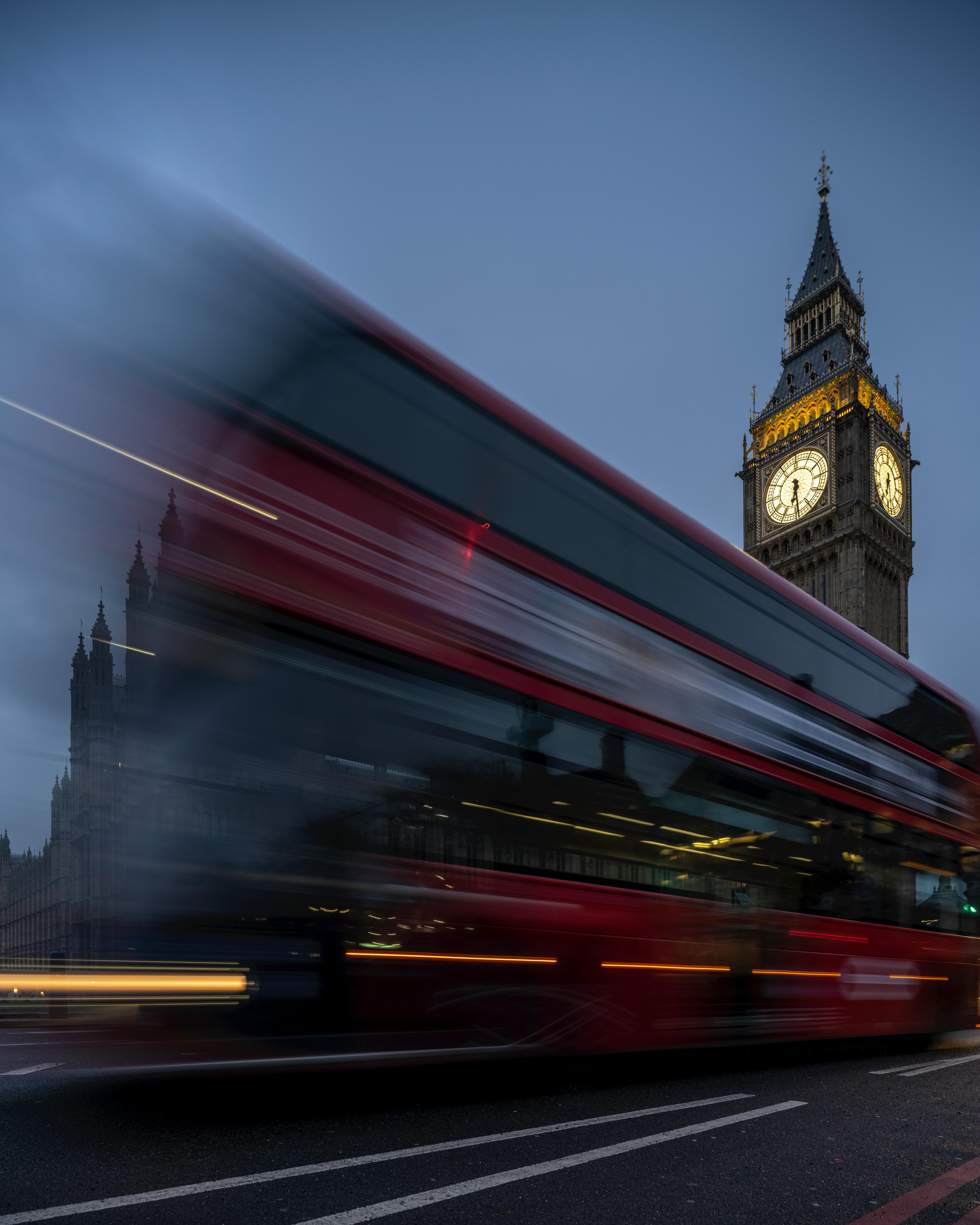 Blurred red bus passing by Big Ben in London at dusk, capturing the city's vibrant atmosphere.