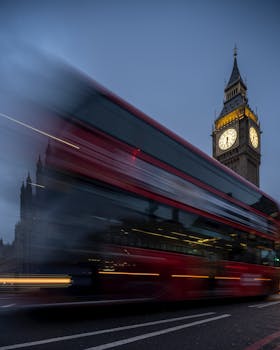 Blurred red bus passing by Big Ben in London at dusk, capturing the city's vibrant atmosphere.