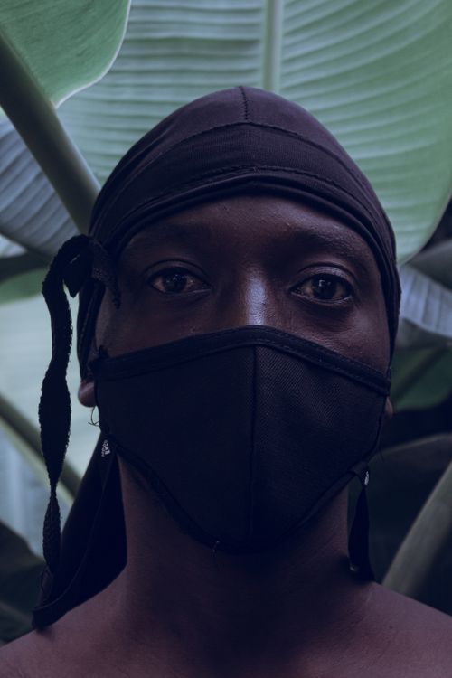 Free Masked individual against lush green leaves, blending fashion and safety. Stock Photo