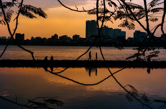 Silhouette of people walking by West Lake at sunset in Hanoi, Vietnam.