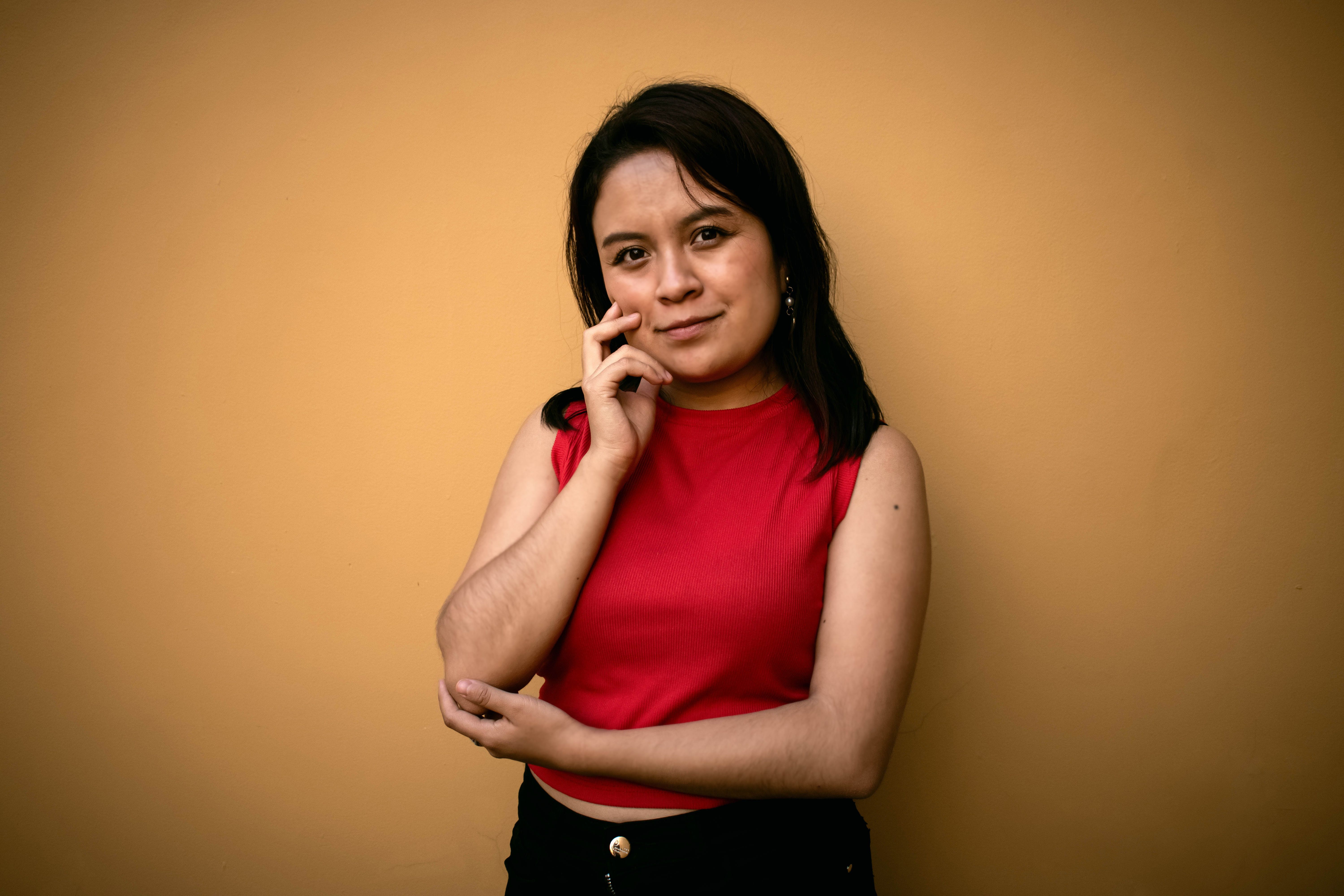 Portrait of a young Hispanic woman in a red top posing confidently against a yellow wall in Puebla, Mexico.