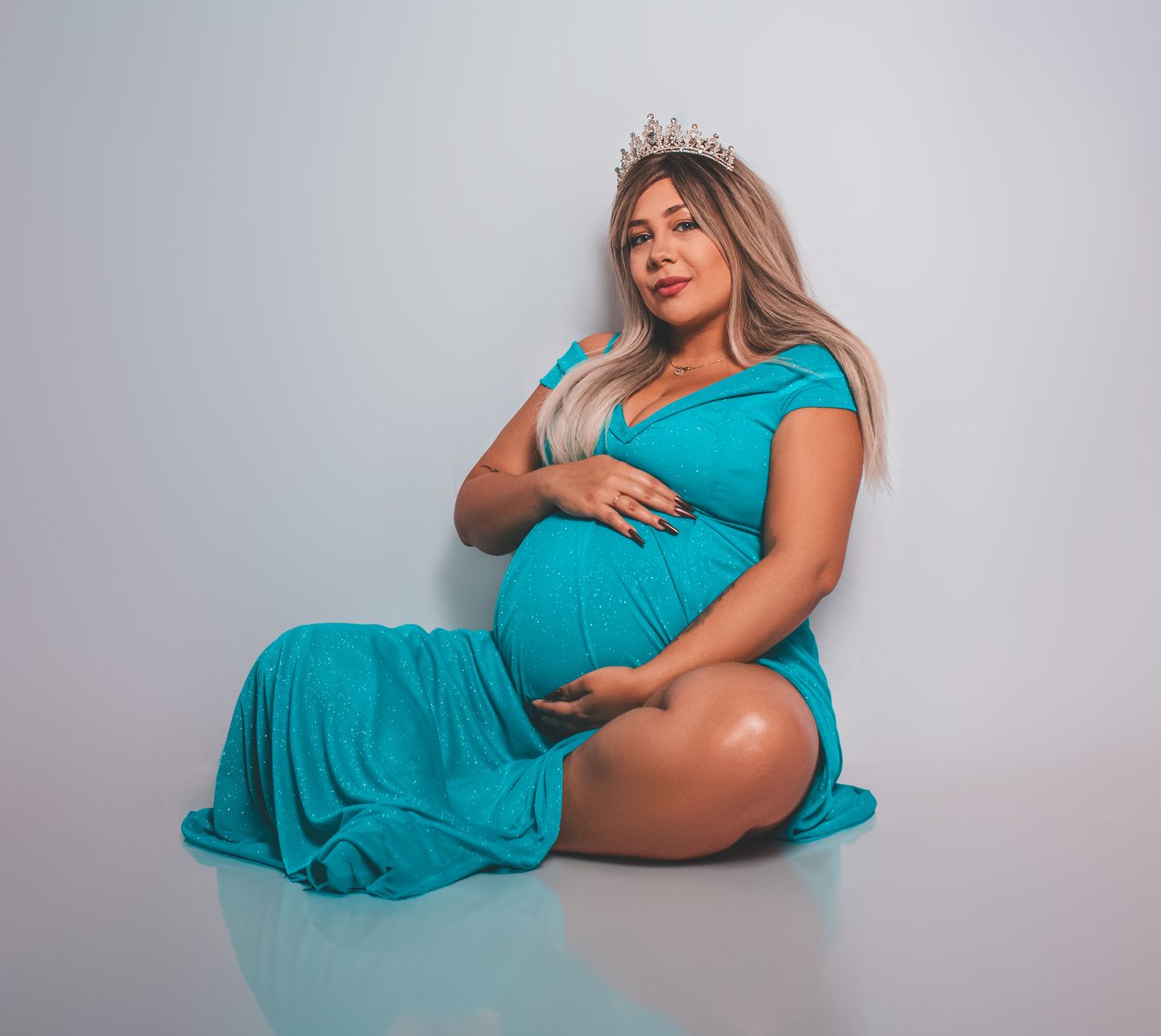 Elegant portrait of a pregnant woman in a blue dress and tiara, exuding beauty and confidence.