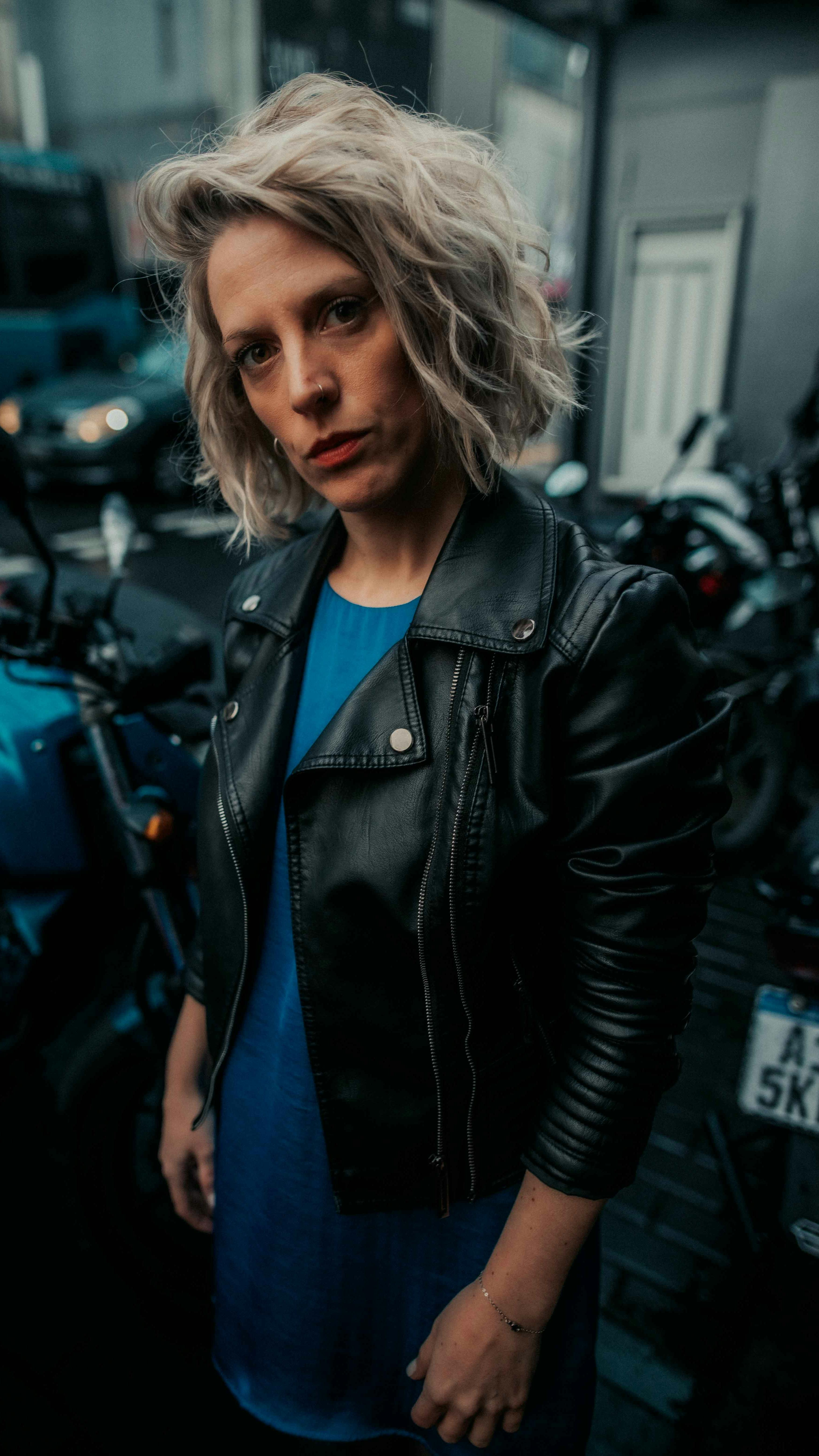 Stylish woman in leather jacket posing confidently on city street at night.