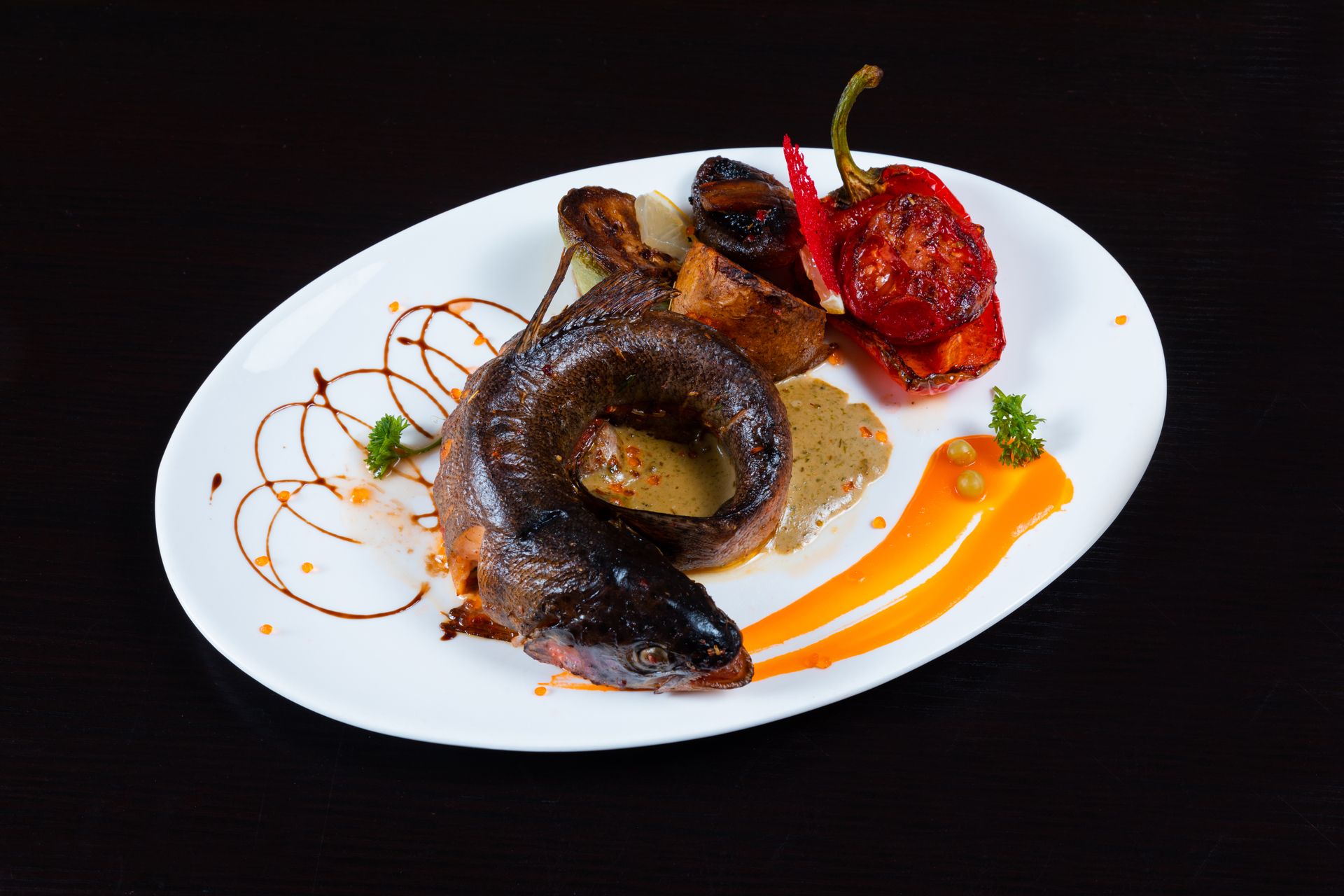 Delicious grilled fish and roasted vegetables on a plate with sauce decor.