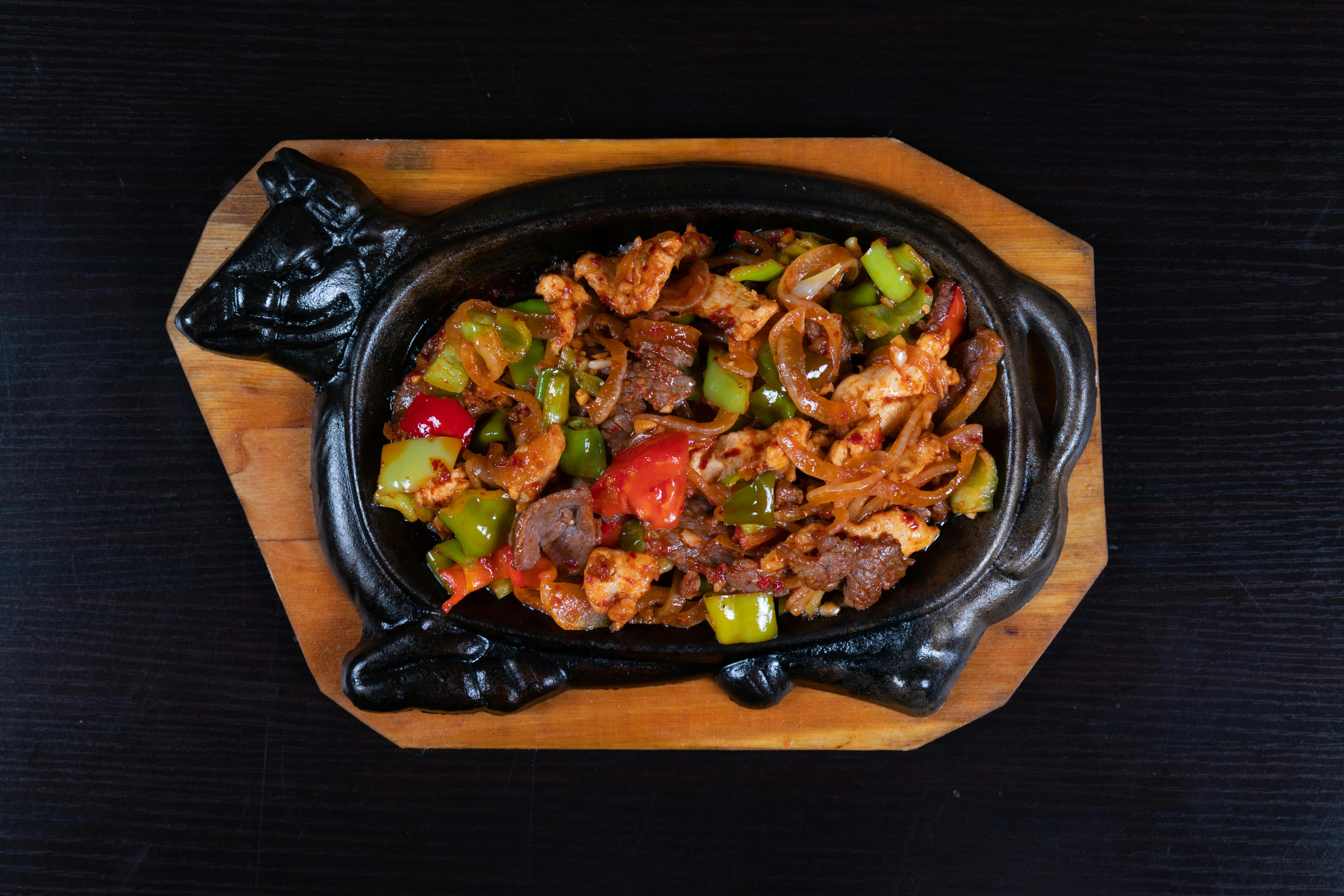 a black dish with meat and vegetables on top